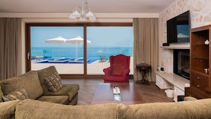 A living room with a large sliding glass door leading to a beach view, a red armchair, a wooden coffee table, and a TV mounted on the wall. - Orient Villas (Zakynthos)