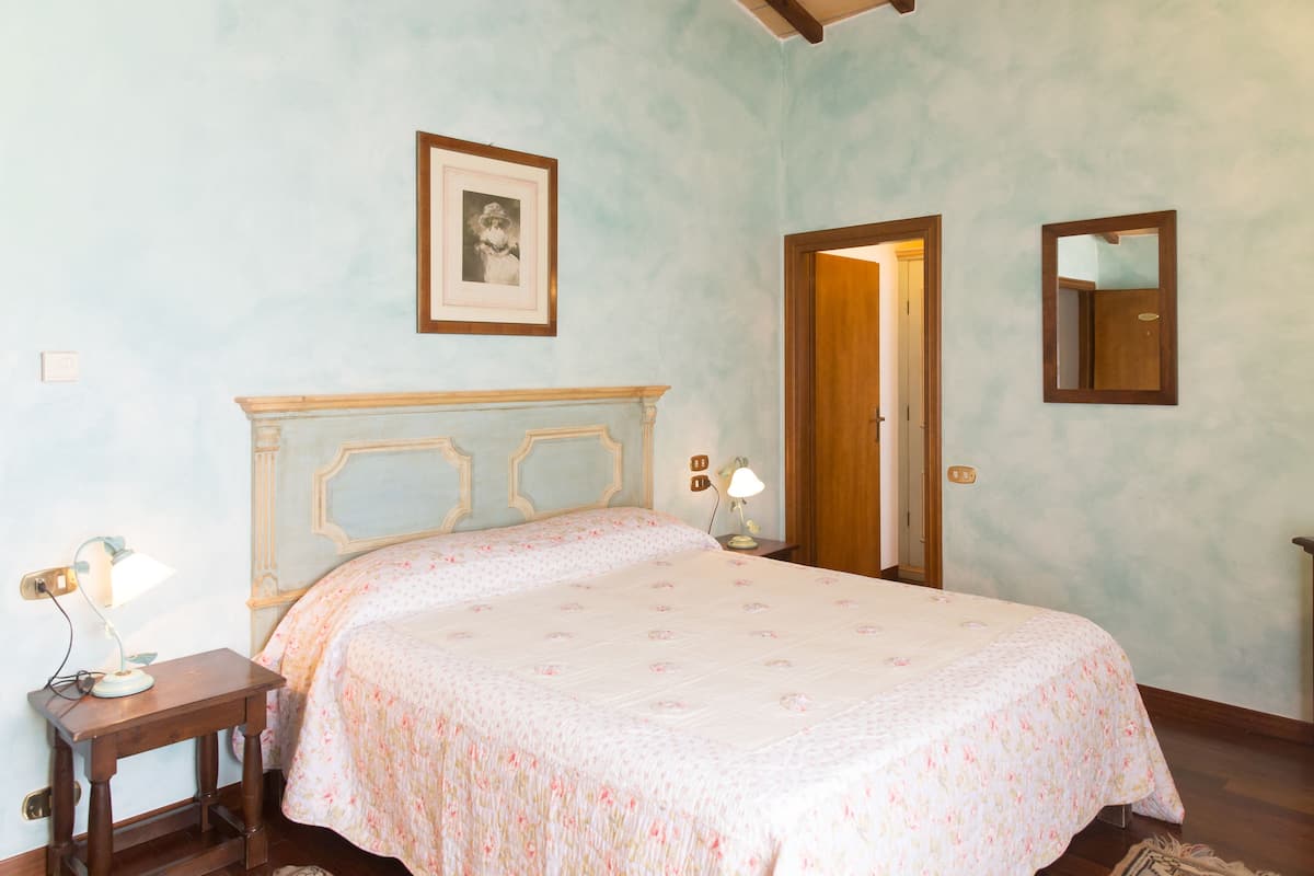 Un dormitorio con cama, mesita de noche, lámpara, cuadro enmarcado y espejo en la pared.
