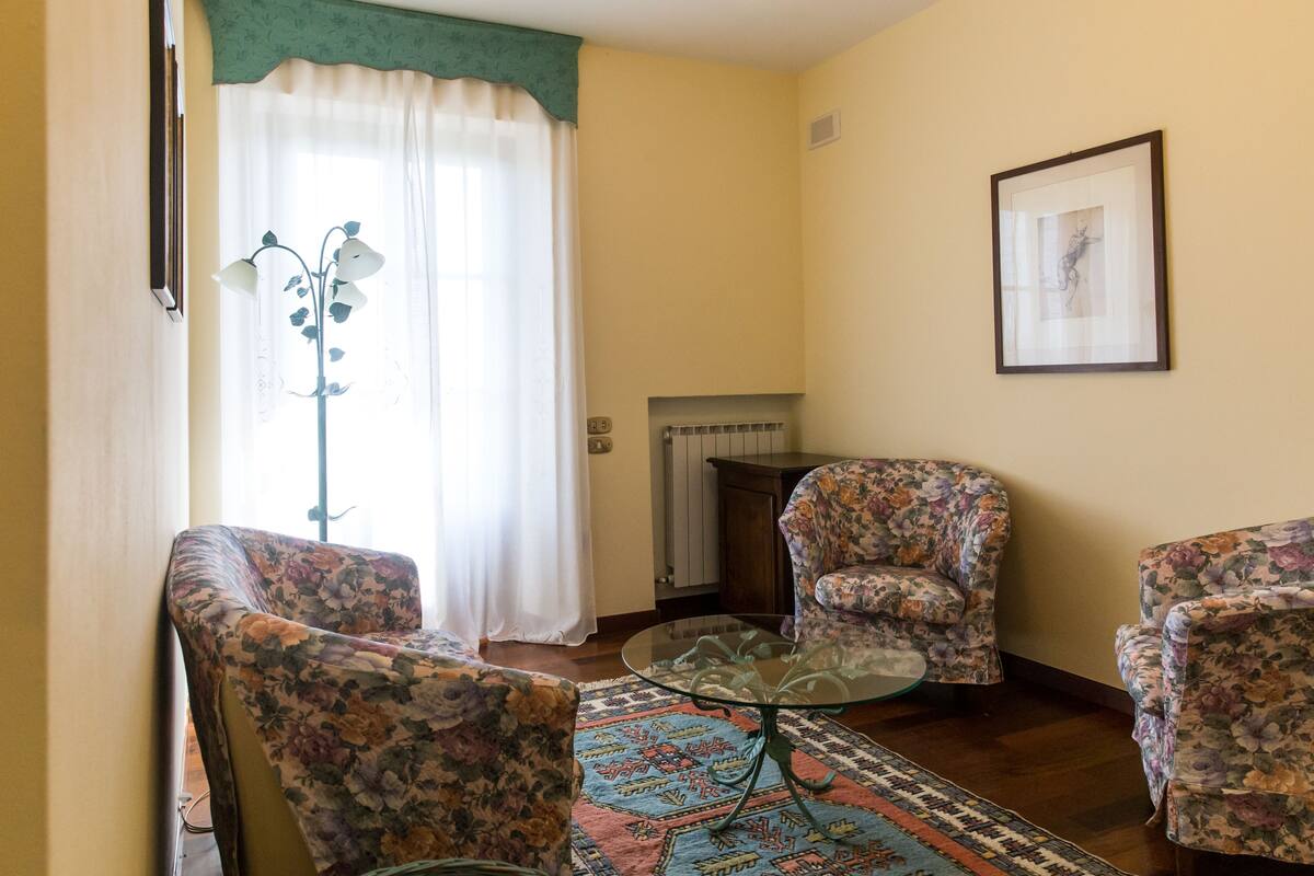 Una sala de estar con sillones de estampado floral, una mesa de centro de vidrio y una alfombra estampada.