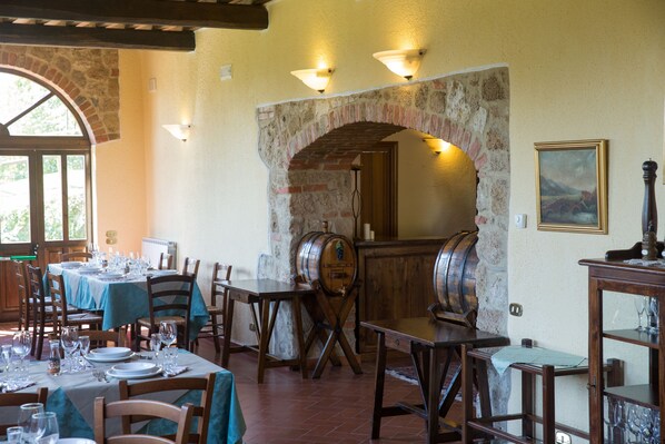 Un comedor con mesas dispuestas para comidas, un arco de piedra y un barril de madera.