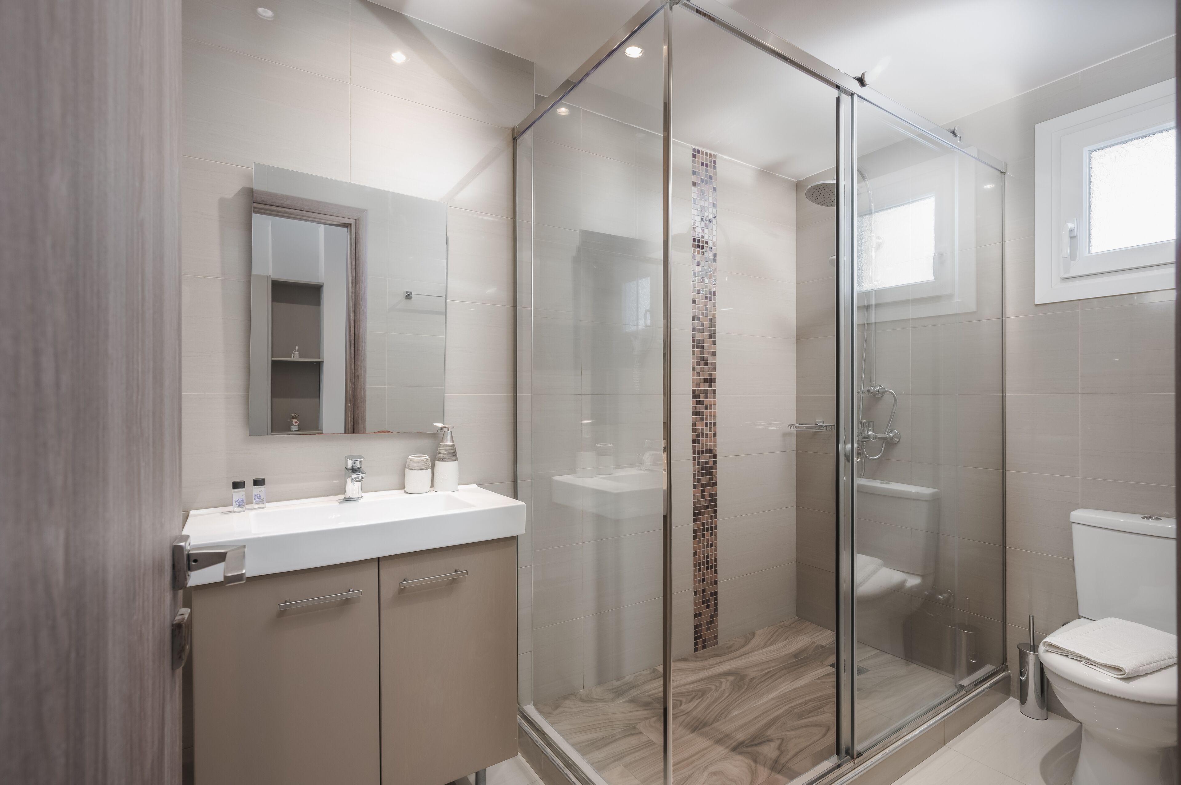 A modern bathroom with a glass-enclosed shower, a white sink, and a toilet.