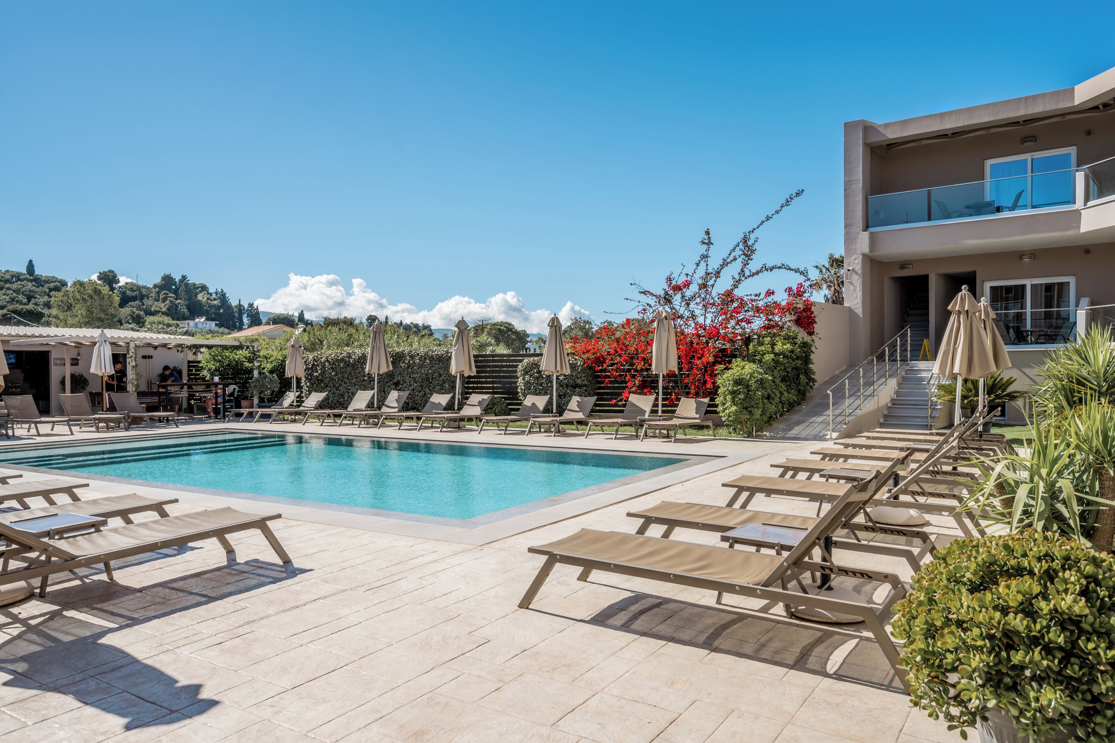 A pool area with lounge chairs, a building with a balcony, and a staircase.