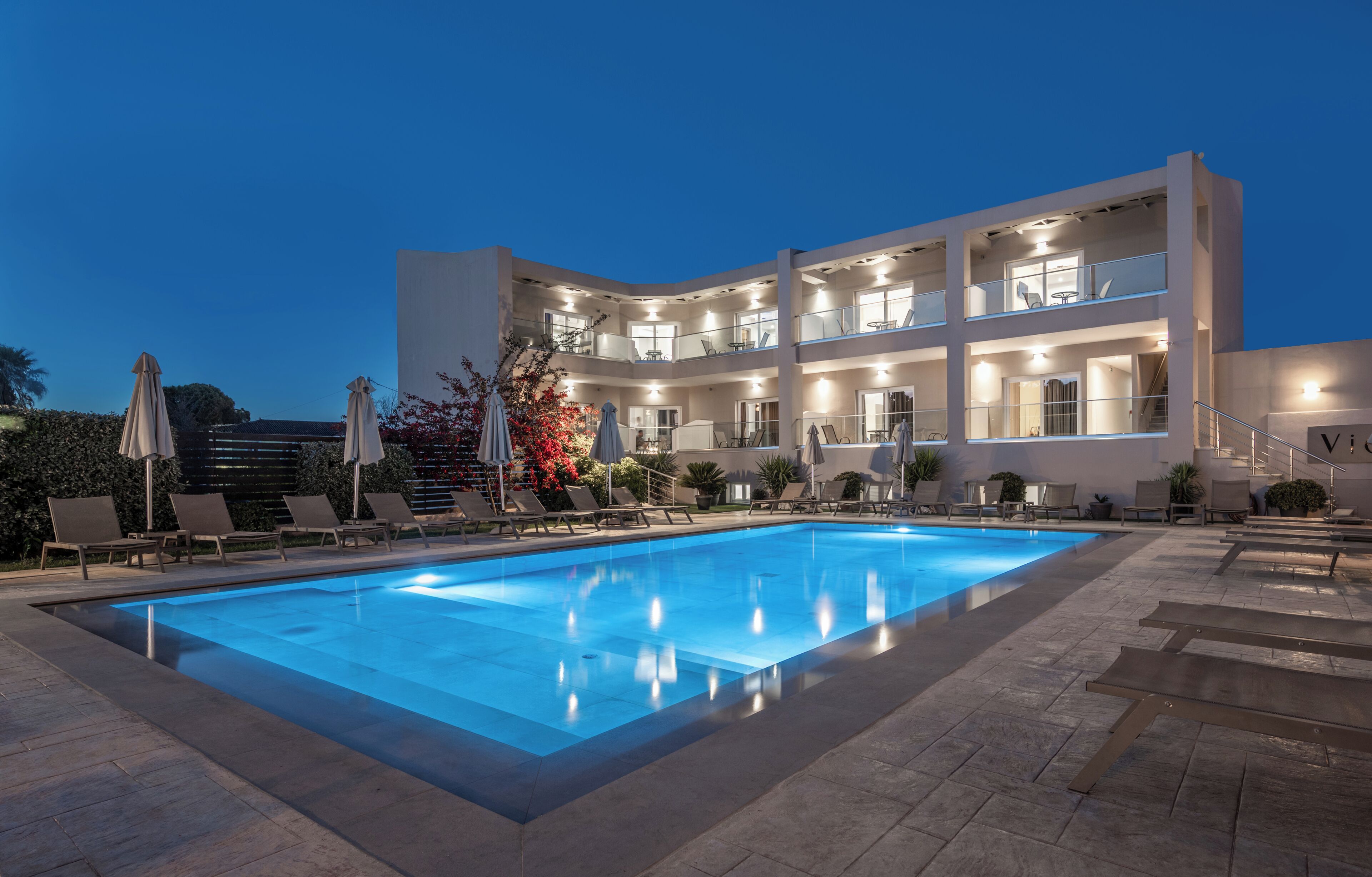 Un hotel de varios pisos con piscina, mobiliario exterior y fachada bien iluminada.