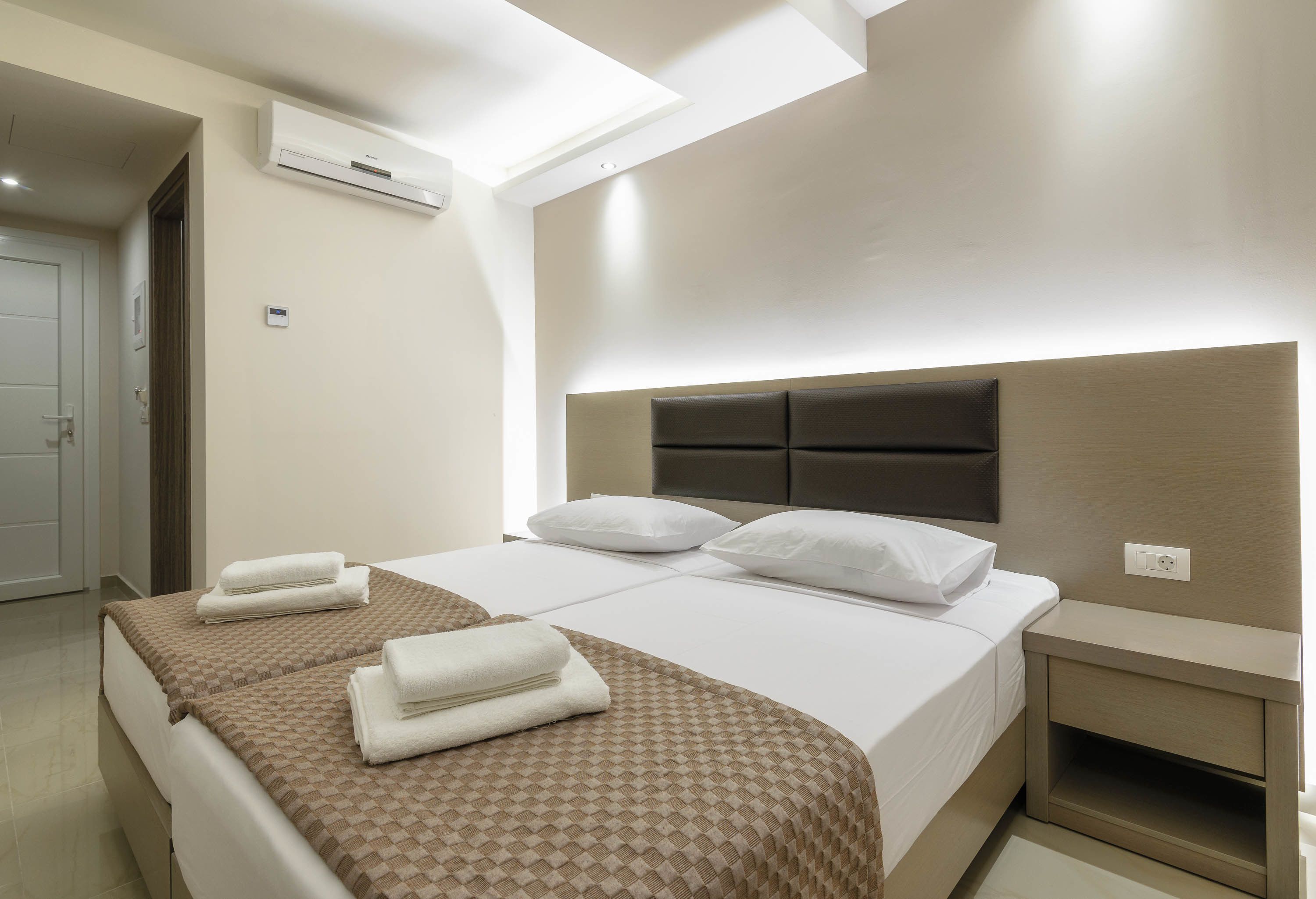 A hotel room with two beds, a bedside table, a nightstand, and an air conditioning unit on the wall.