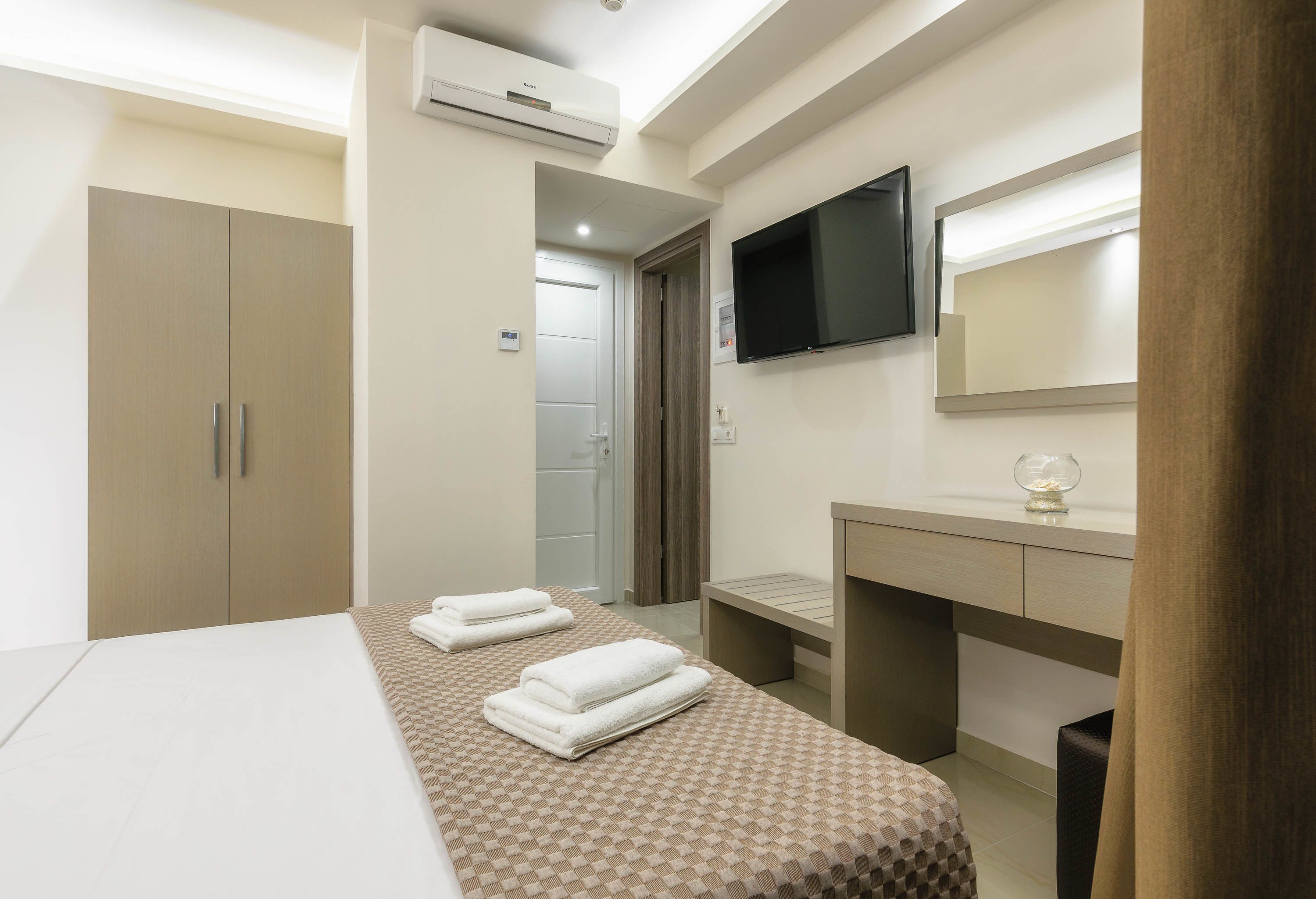 Una habitación de hotel con una cama, un televisor montado en la pared, un espejo y una mesita con un objeto decorativo.