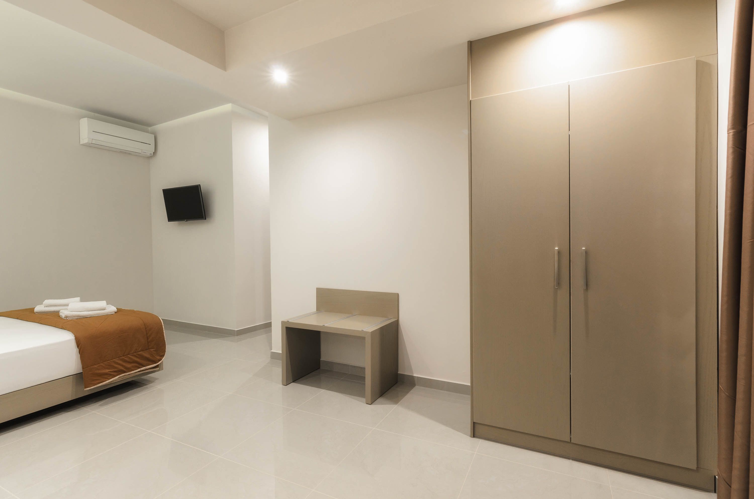 A modern hotel room with a bed, a small table, a TV mounted on the wall, and a wardrobe.