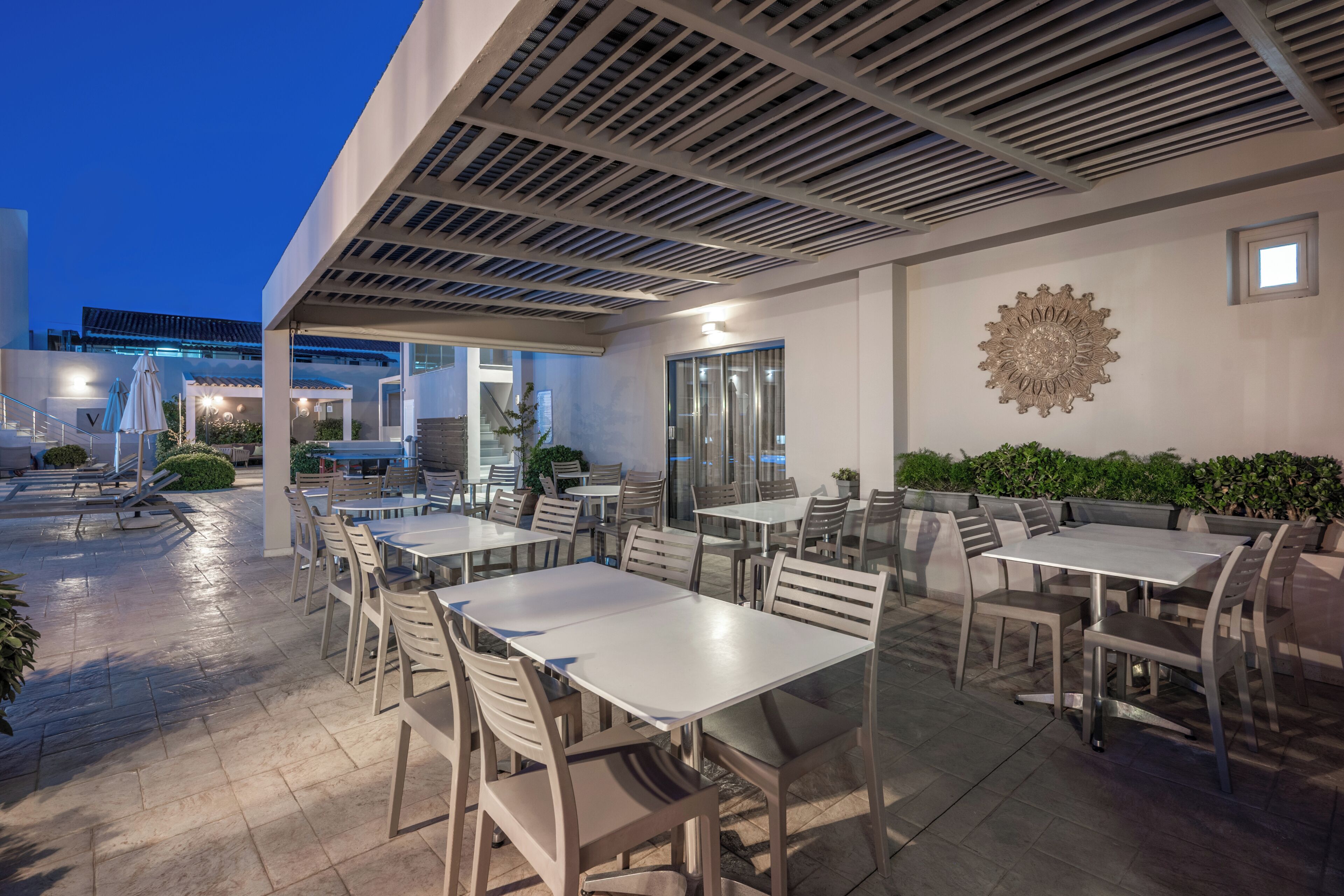An outdoor dining area with tables and chairs, a ceiling with a grid pattern, and a decorative wall piece.