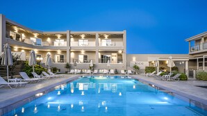 Un hotel moderno con piscina, varios balcones y zonas de estar con sombrillas.