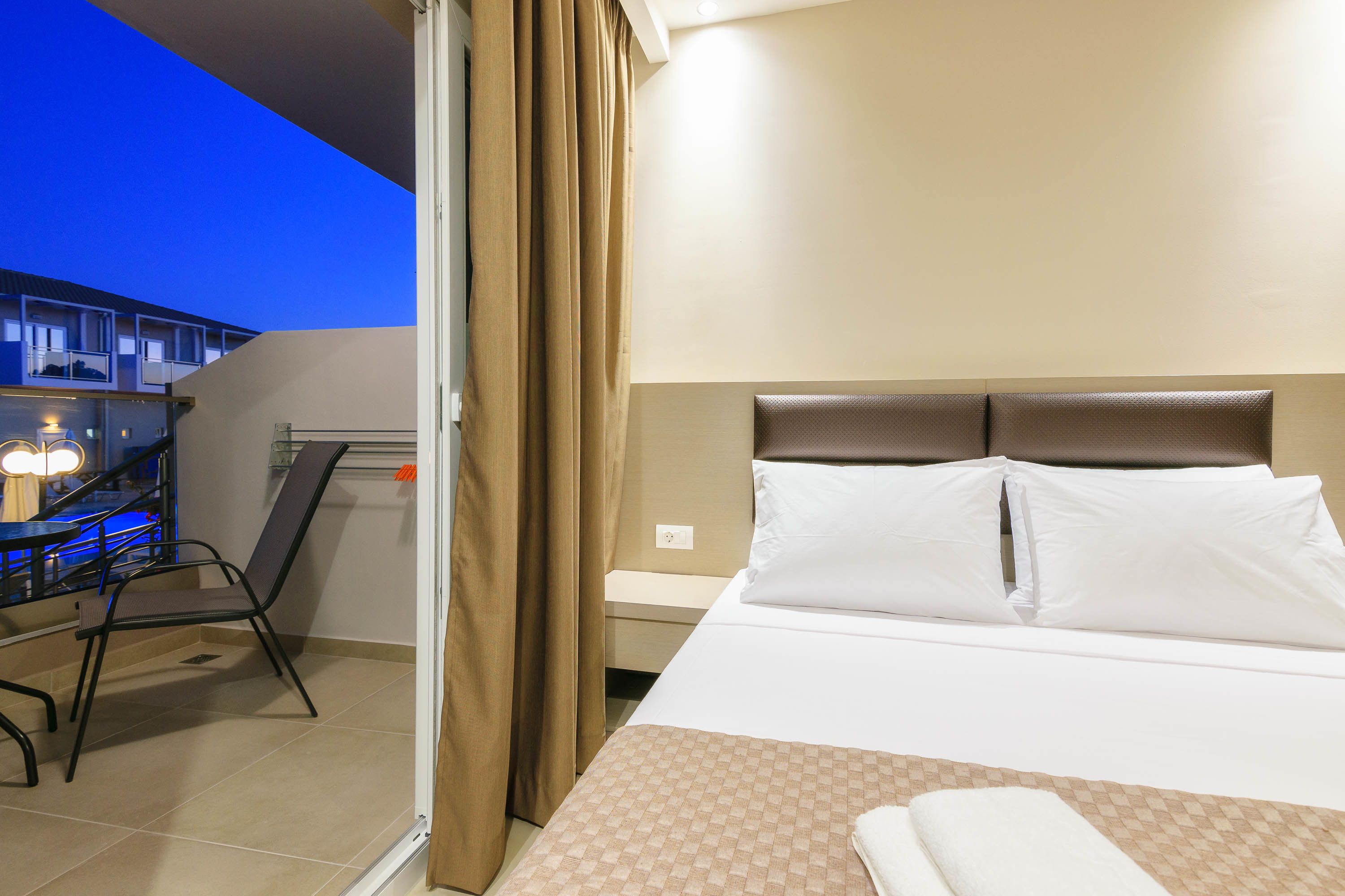 A hotel room with a bed, a chair, a desk, and a view of the outside.