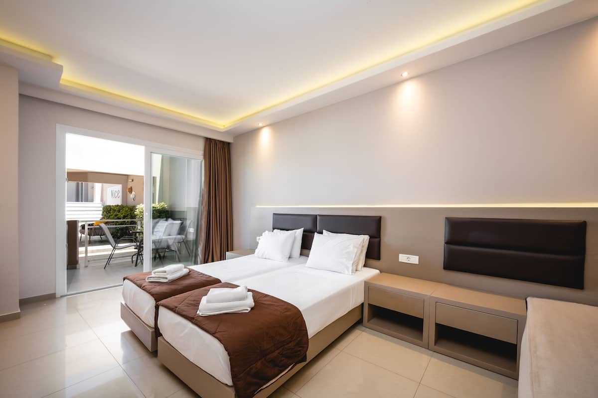 Una habitación de hotel moderna con una cama grande, una mesita de noche, un televisor de pantalla plana en la pared y una puerta corrediza de vidrio que da a un balcón.