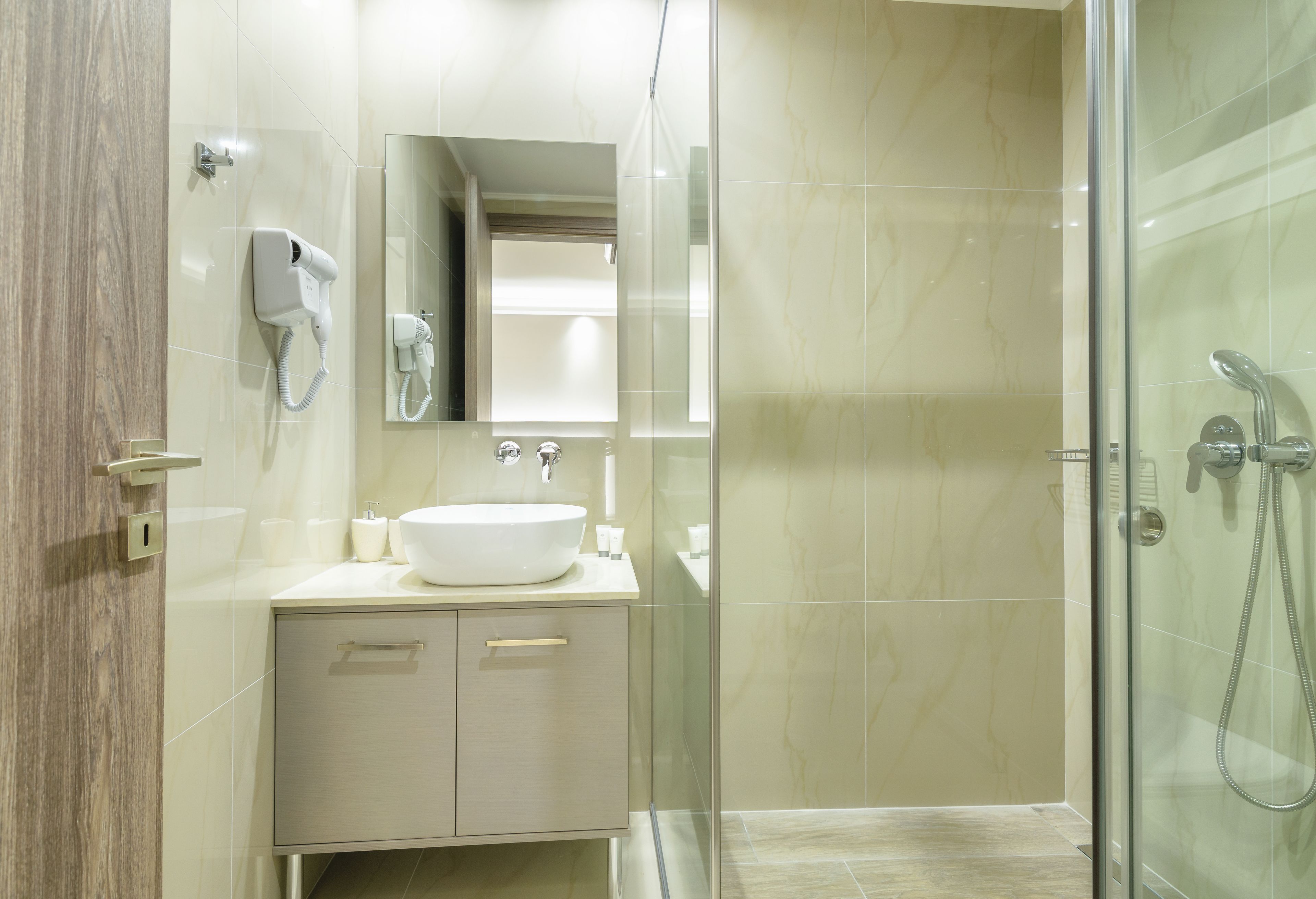 Un bagno moderno con doccia vetrata, un mobile lavabo con lavandino e specchio, e un asciugacapelli fissato alla parete.