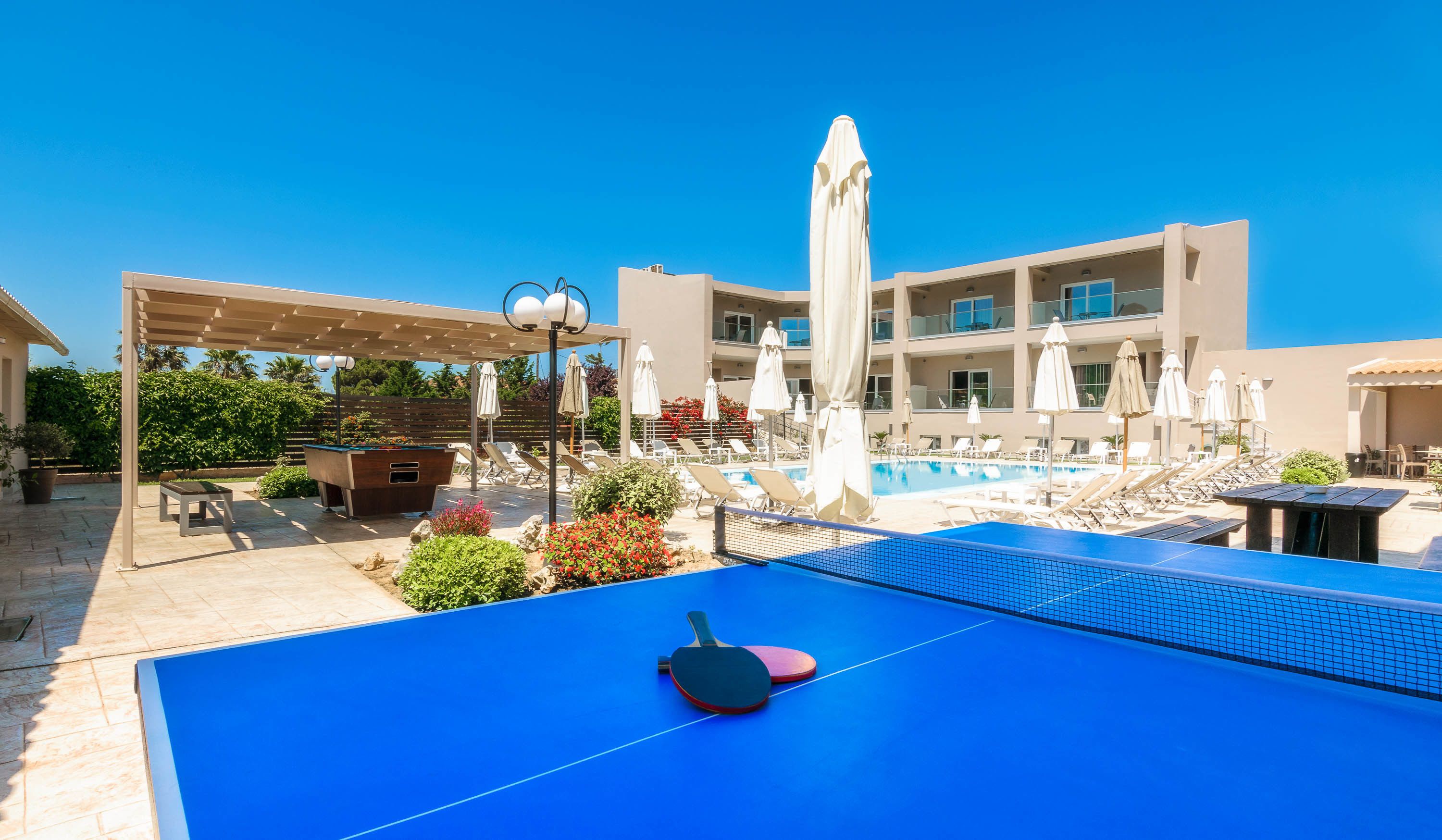 A rooftop pool area with lounge chairs, umbrellas, and a ping pong table.