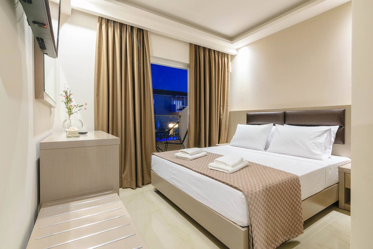 Habitación de hotel con cama, mesita de noche, cortinas y vistas al exterior.