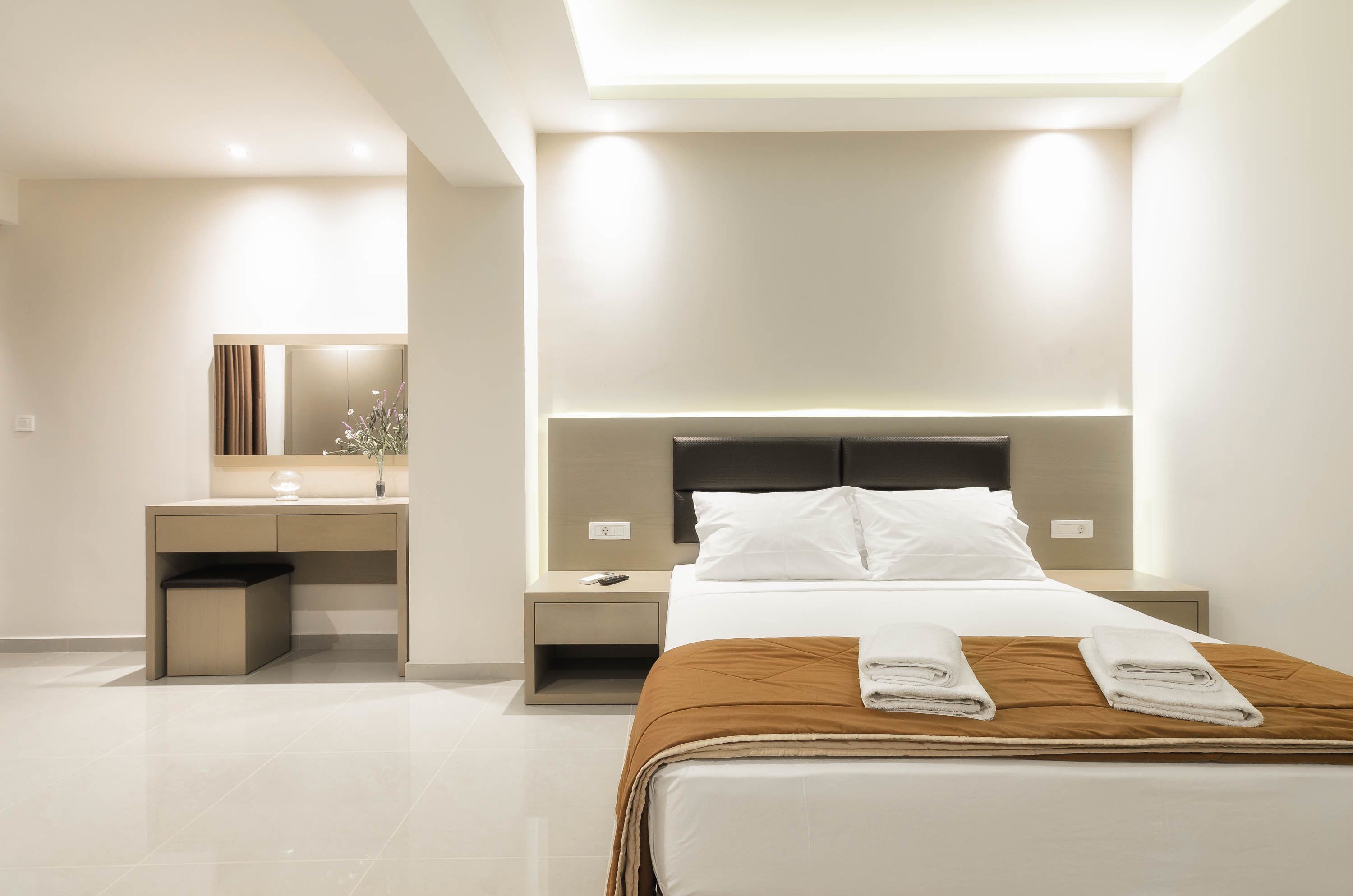 A modern hotel room with a neatly made bed, a bedside table, a nightstand, a desk, and a mirror.