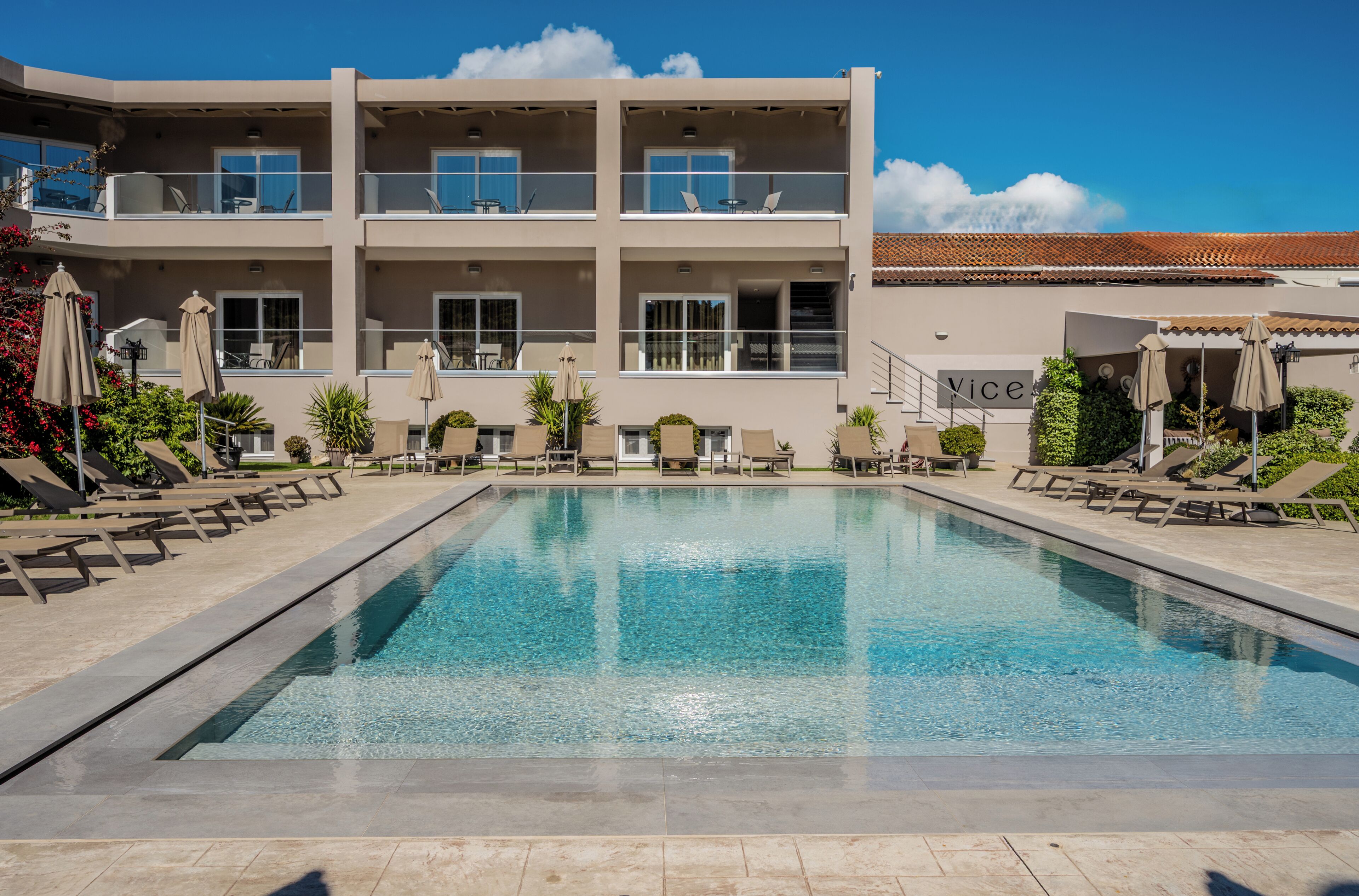 Un hôtel moderne doté d’une piscine, de chaises longues et d’un espace extérieur aménagé pour se détendre.