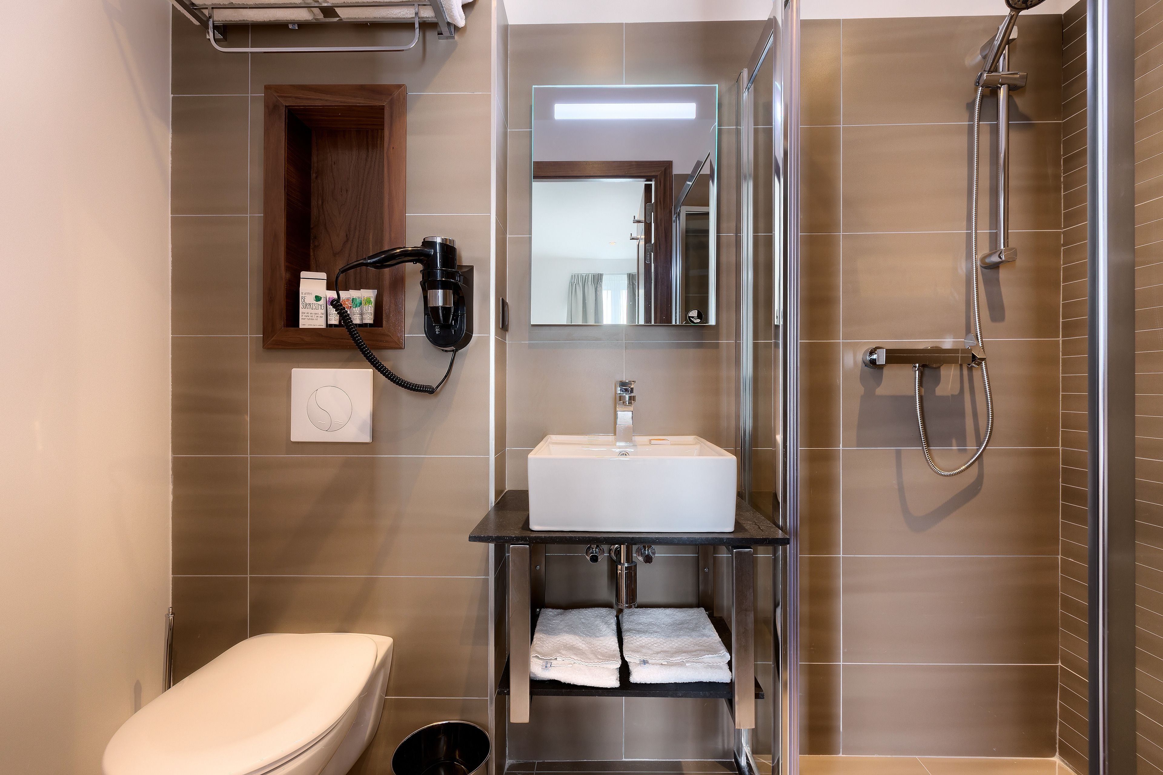 Un baño moderno con inodoro, lavamanos, espejo y ducha.
