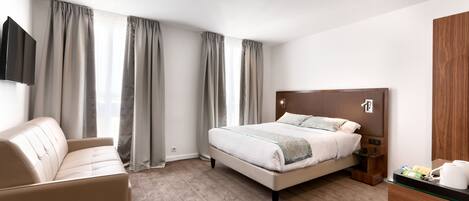 A modern hotel room with a bed, a sofa, a TV, and a wooden cabinet.