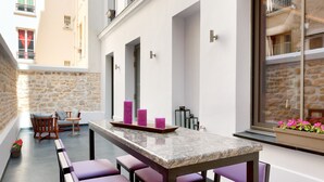 Een moderne buiten eethoek met een marmeren tafel, paars zitmeubilair en een stenen achtergrondmuur.