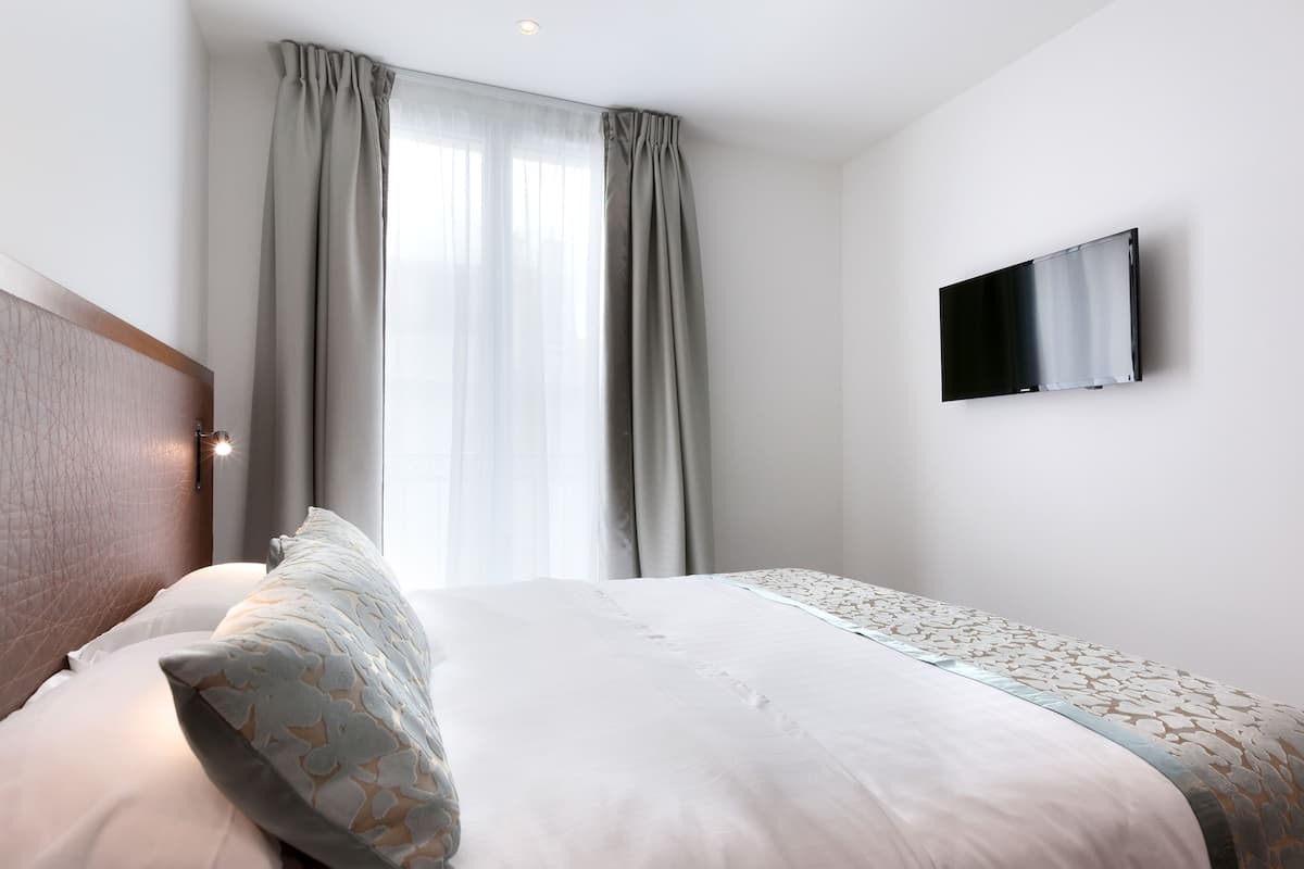 A hotel room with a bed, curtains, a mounted TV, and a headboard.