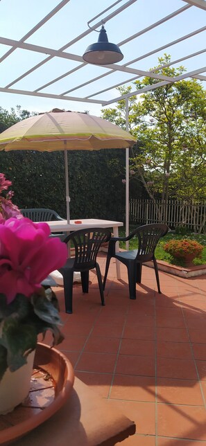 Une terrasse extérieure avec une table et des chaises, une lampe suspendue et des plantes en pot.