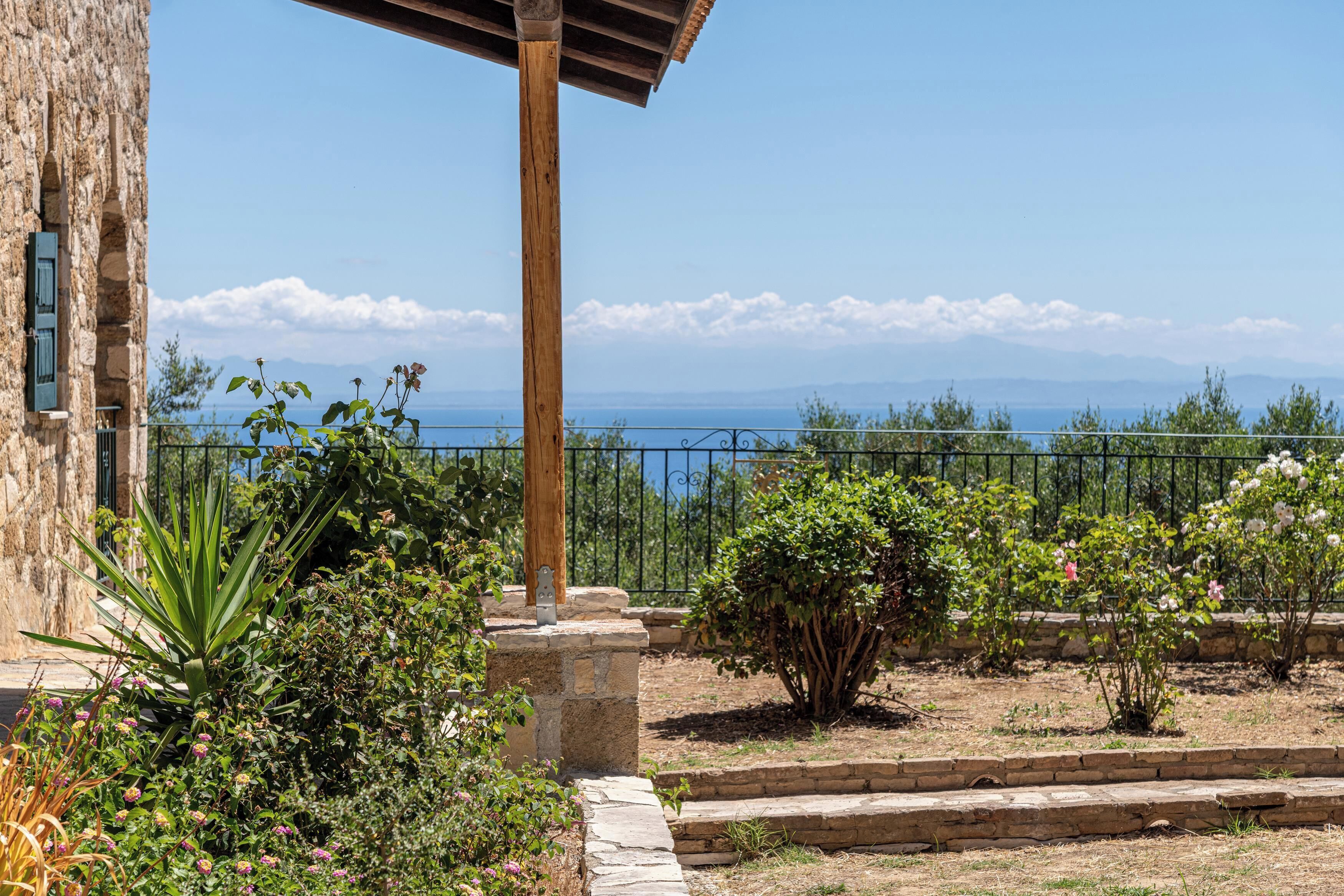 A stone building with a wooden pergola, a metal fence, and a view of the sea.