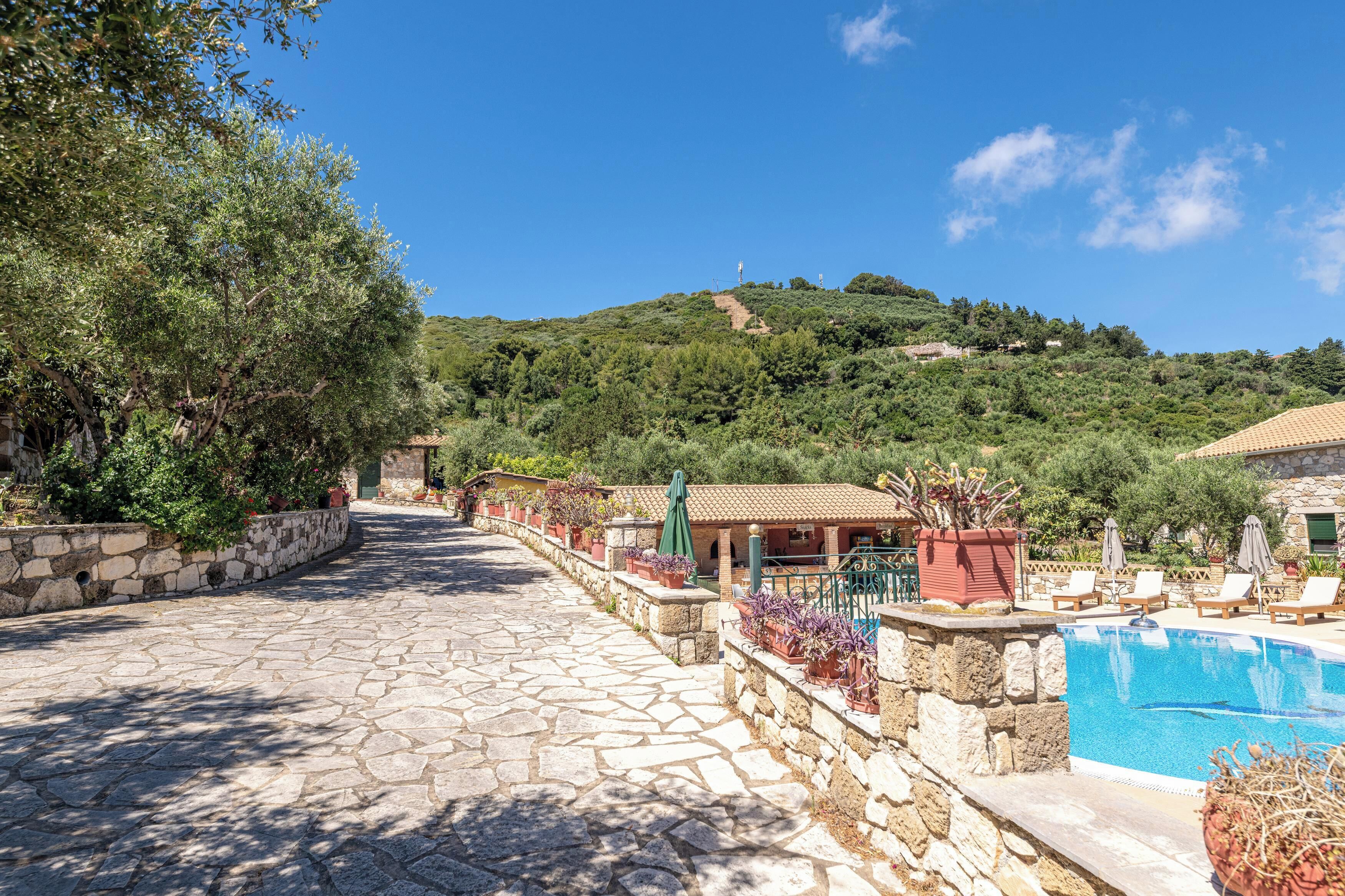 A stone-paved pathway leading to a pool area with a view of a hillside.
