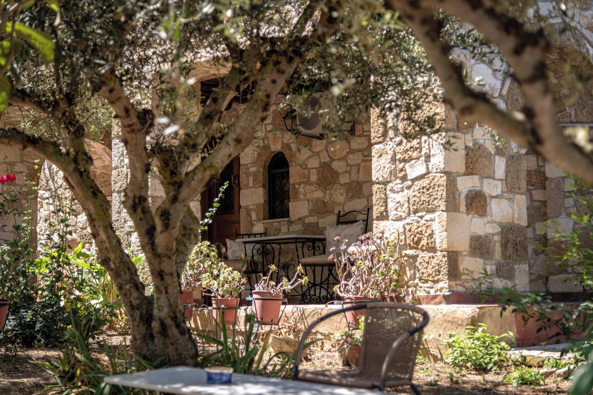 An outdoor seating area with stone walls, potted plants, and a tree providing shade.
