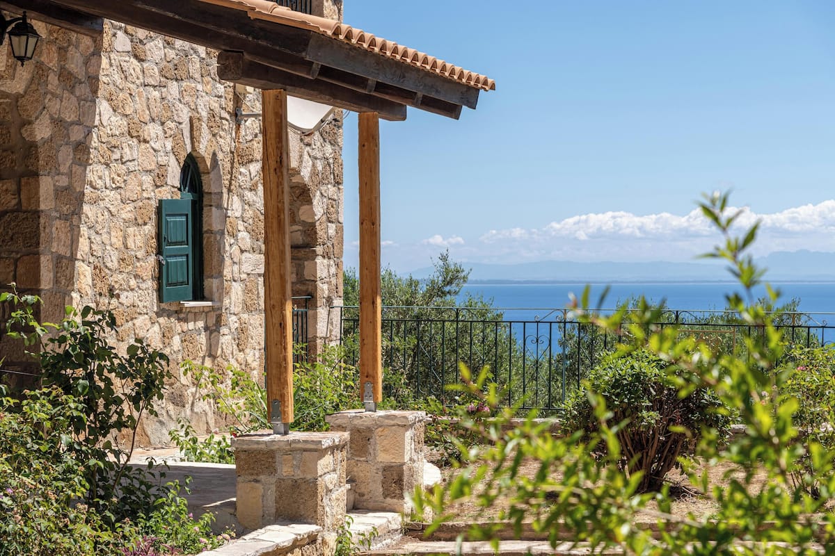 A stone building with a wooden balcony, a green door, and a view of the sea.