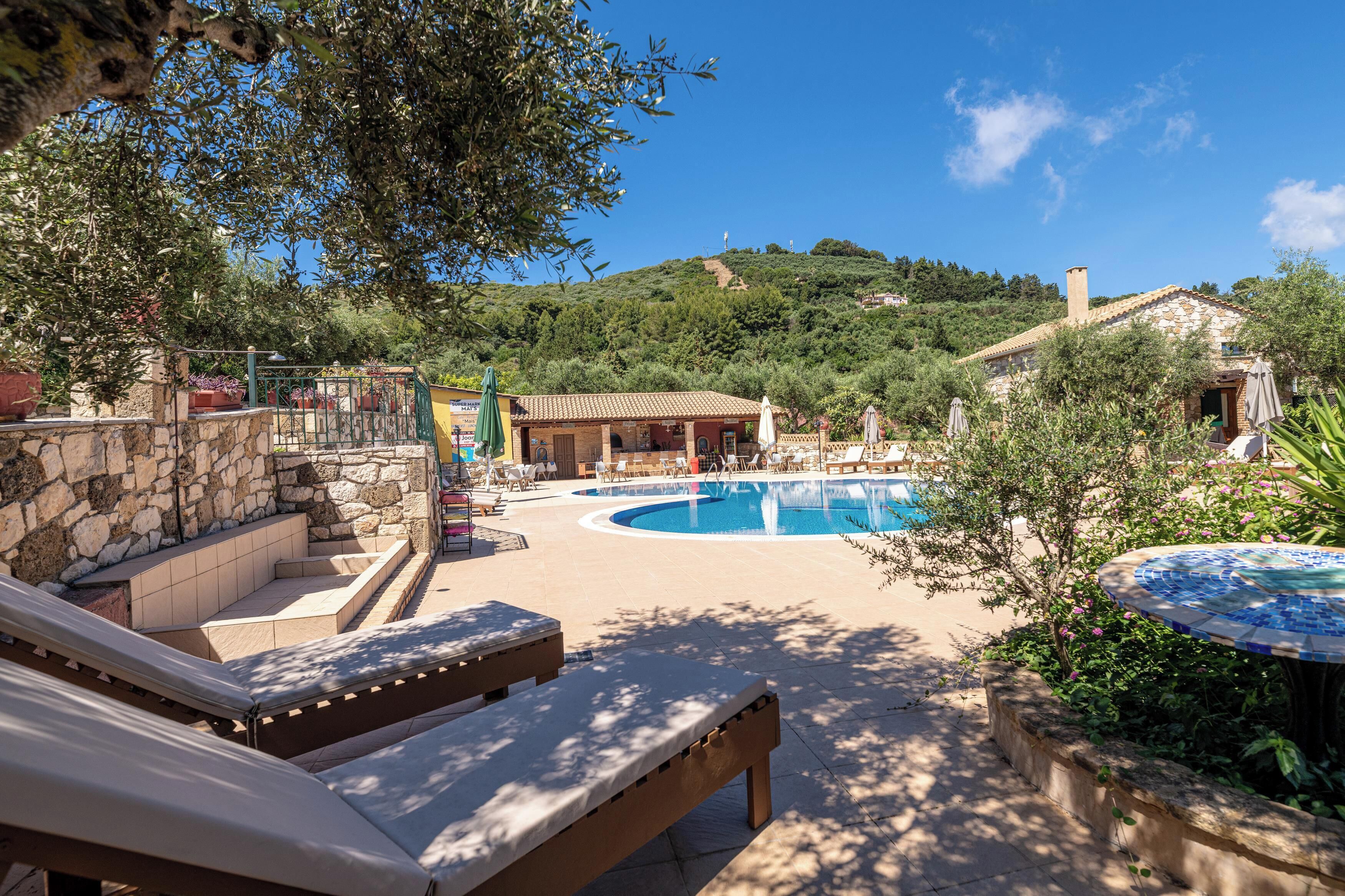 A pool area with lounge chairs, a stone wall, and a view of a hillside.