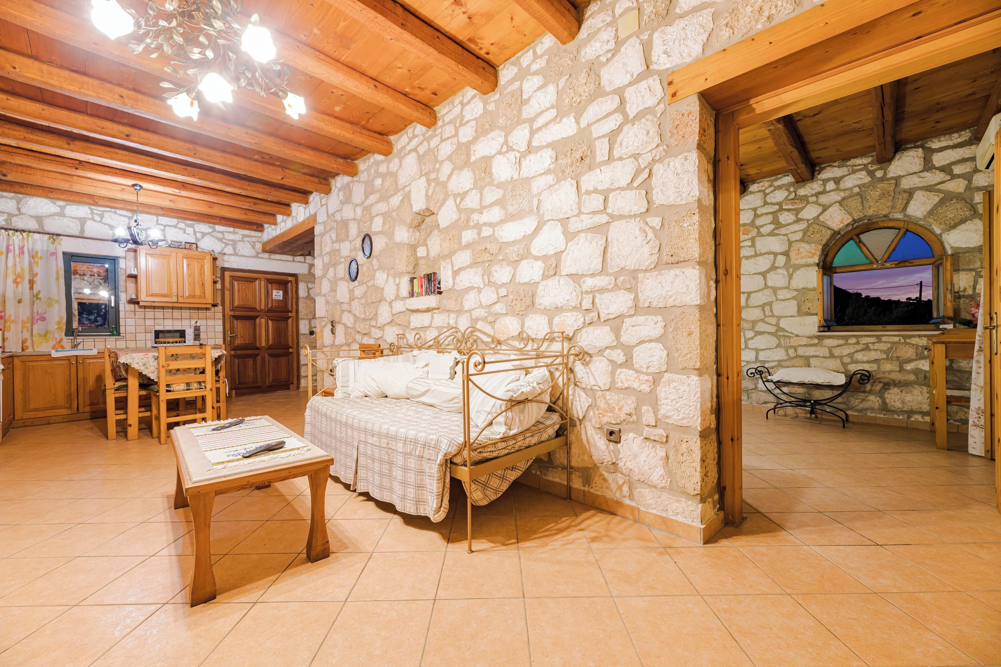 A rustic stone-walled room with a bed, wooden furniture, and a stone fireplace.