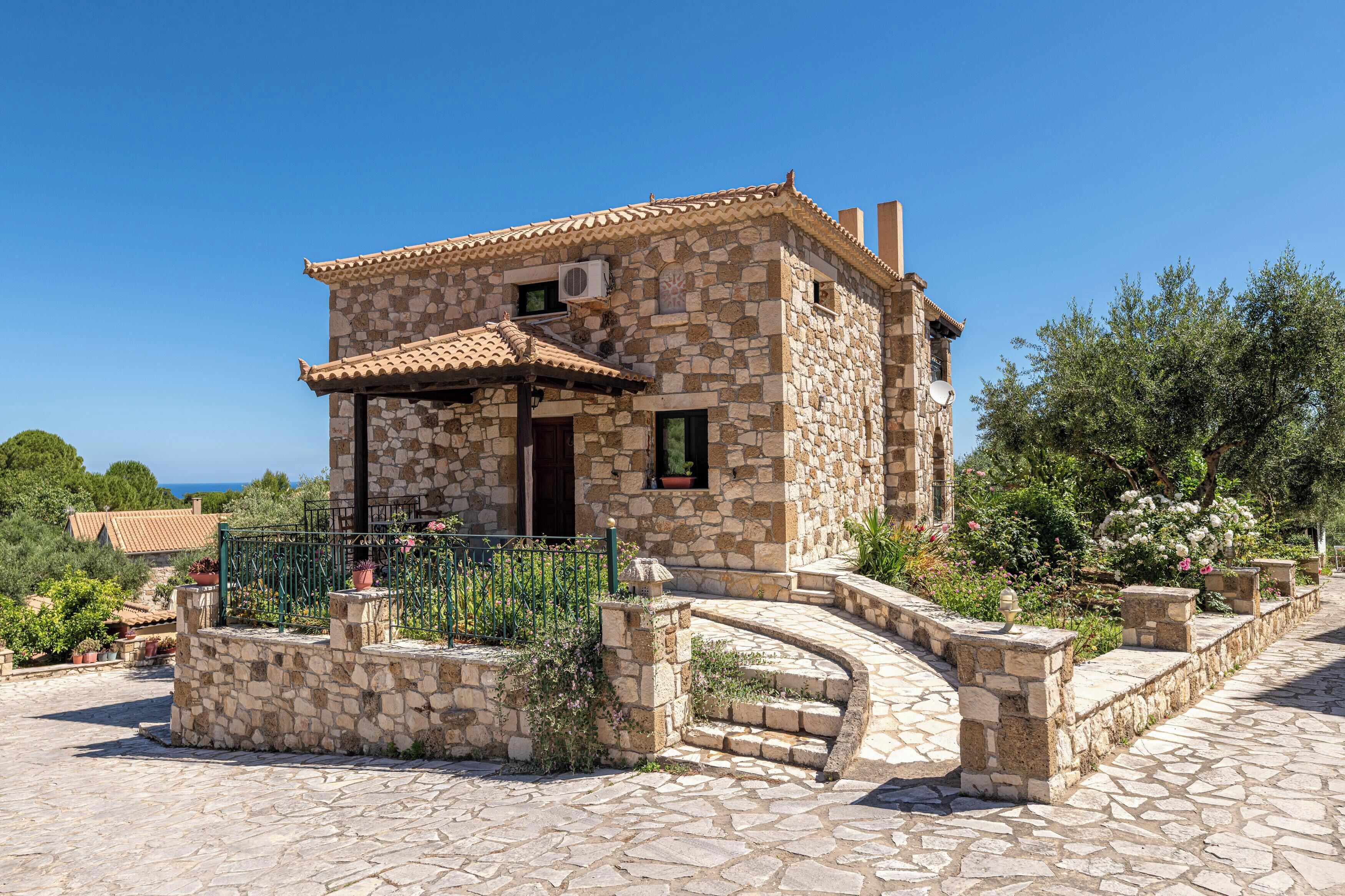 A stone building with a tiled roof, a small porch, and a stone pathway leading to the entrance.