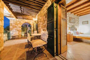 A stone-walled room with a bed, a table with chairs, and a small balcony.