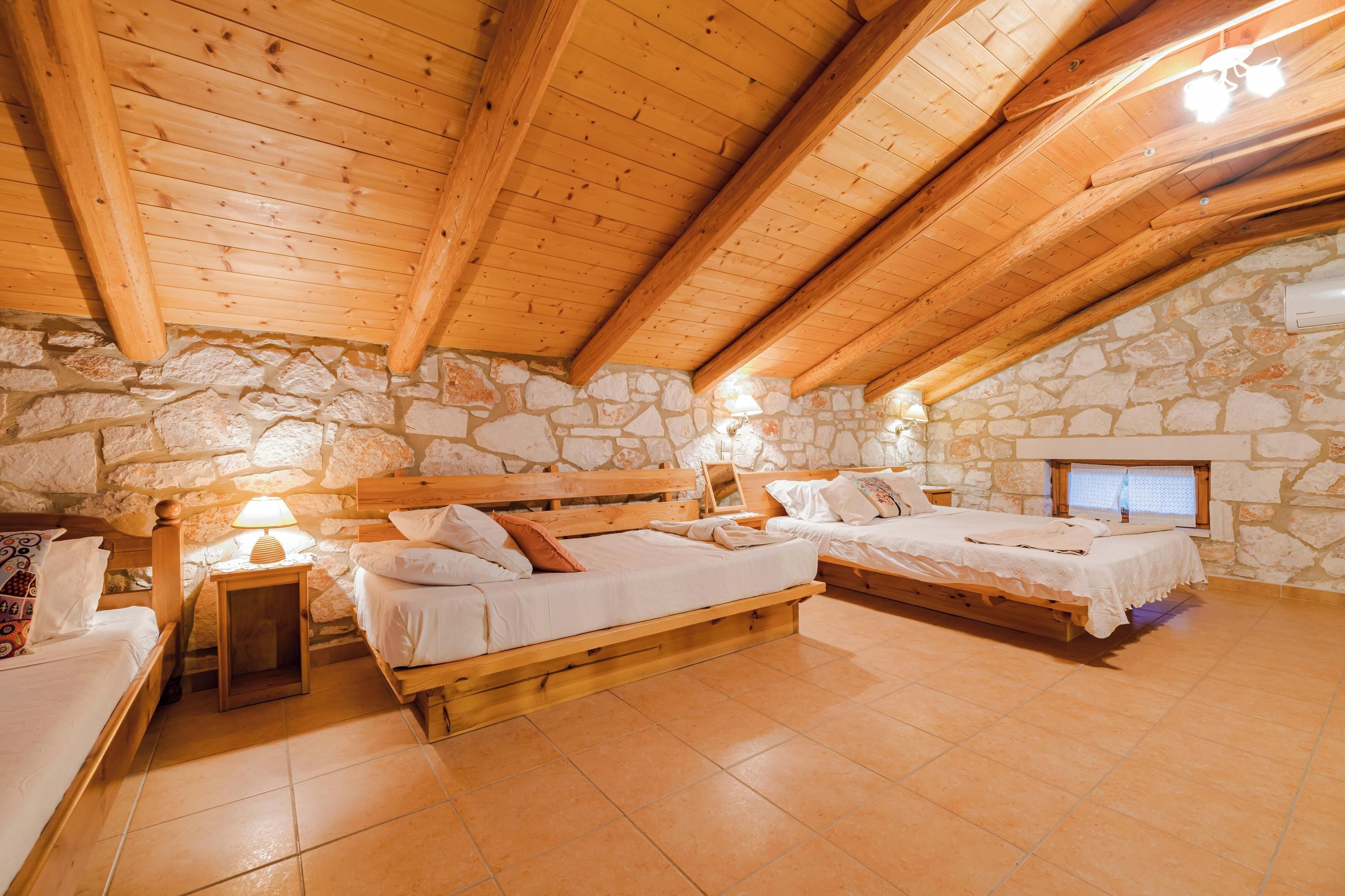 A cozy attic bedroom with stone walls, wooden beams, and two beds.