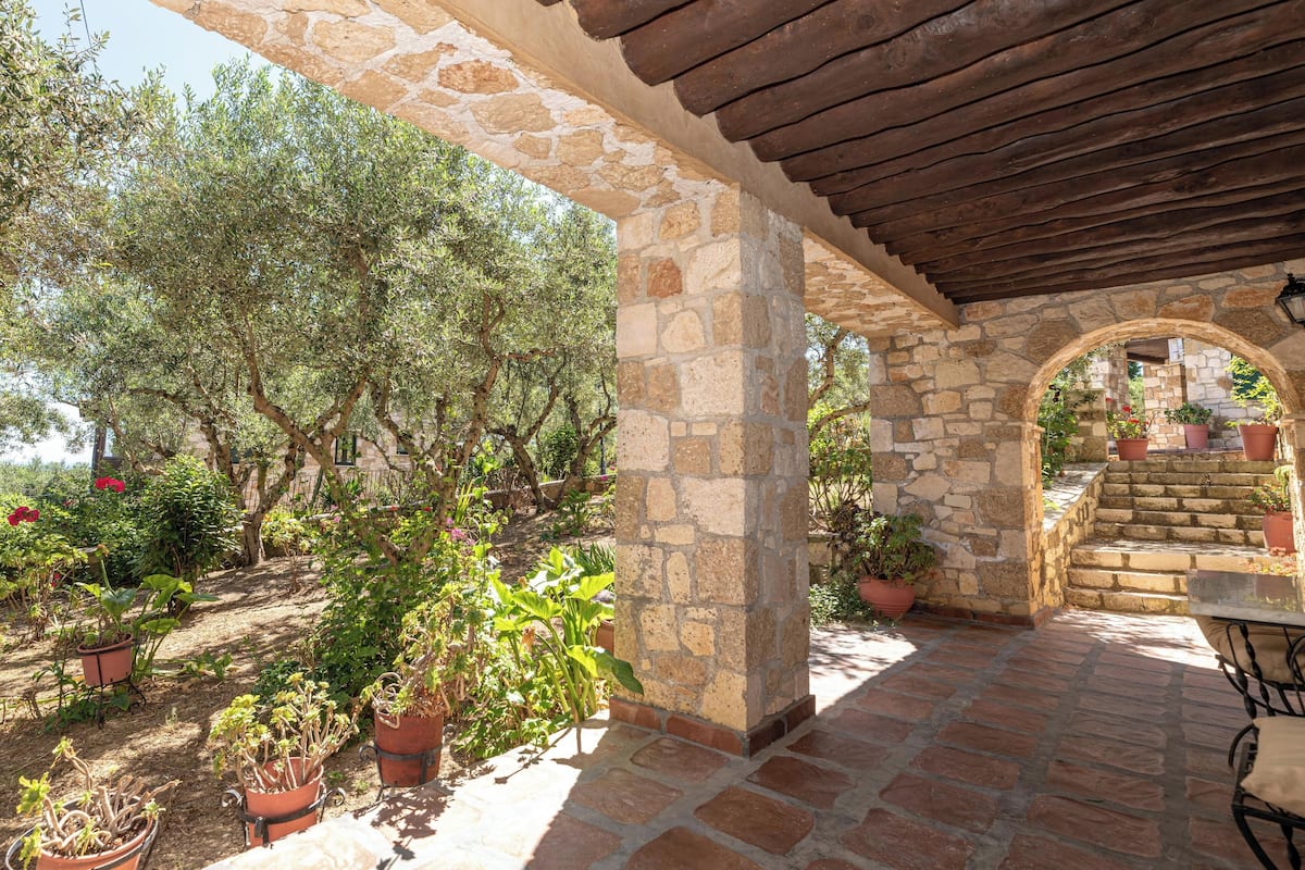 A stone courtyard with potted plants, a pergola, and a staircase leading to an upper level.