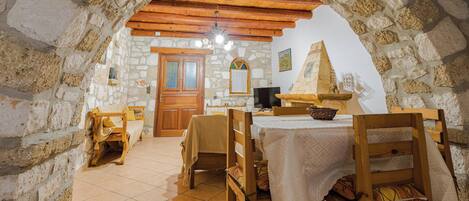 Un comedor con paredes de piedra, muebles de madera, suelo de baldosas y techo de madera.