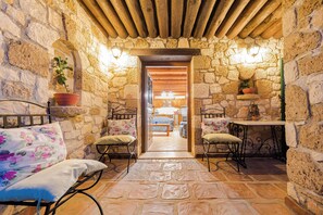 A stone-walled room with a bed, two chairs, a table, and a hanging light fixture.