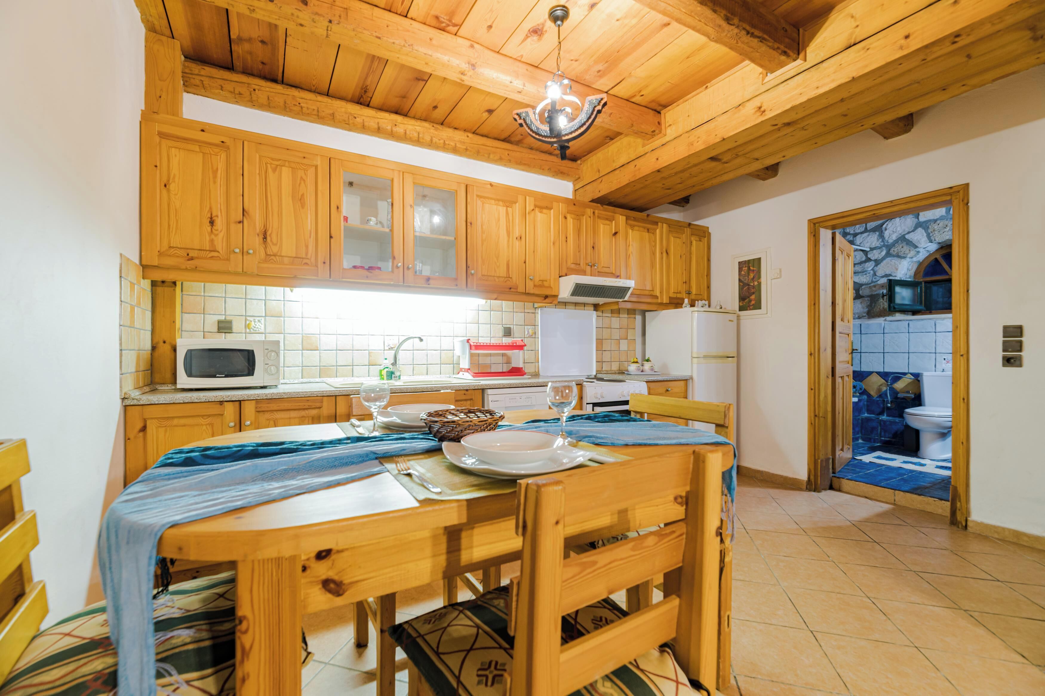 A wooden kitchen with a dining table set for two, a microwave, and a stone-tiled bathroom visible through an open door.