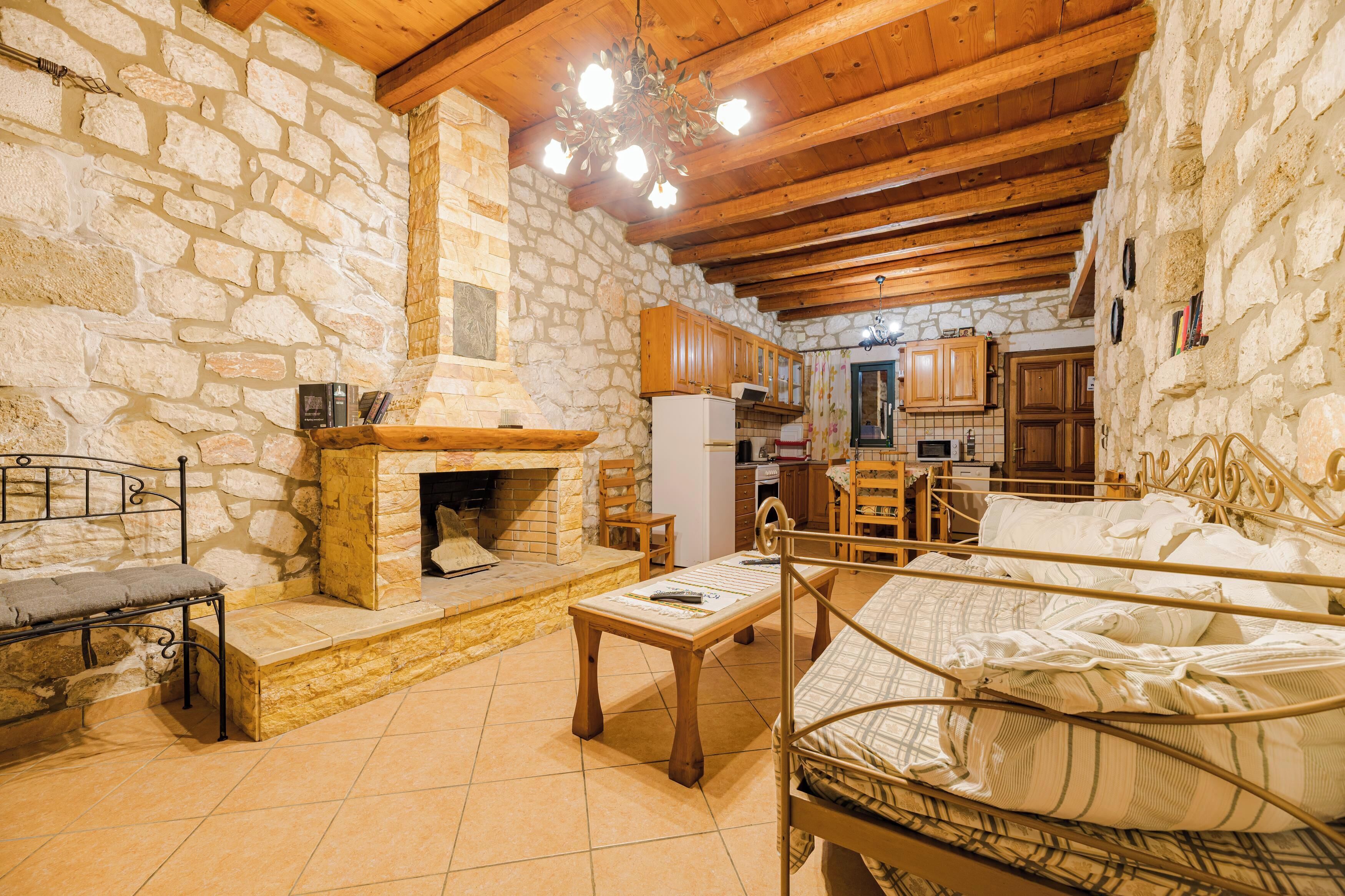 A rustic stone-walled room with a bed, a table, a bench, and a fireplace.