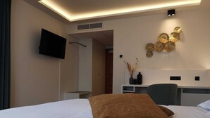 A hotel room with a bed, a desk, a chair, a flat-screen TV mounted on the wall, and a decorative wall piece. - Kasteel van Nieuwland (Aarschot)