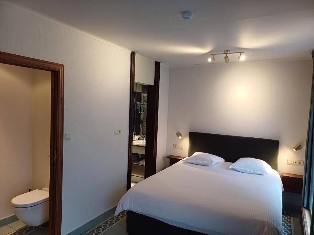A hotel room with a bed, bedside tables, a mirror, and a bathroom with a toilet and sink.