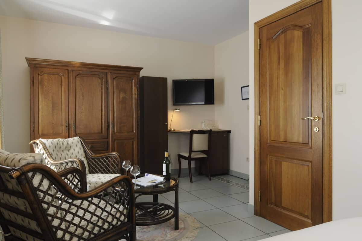 A living room with a sofa, two armchairs, a coffee table, a television, a cabinet, and a door.