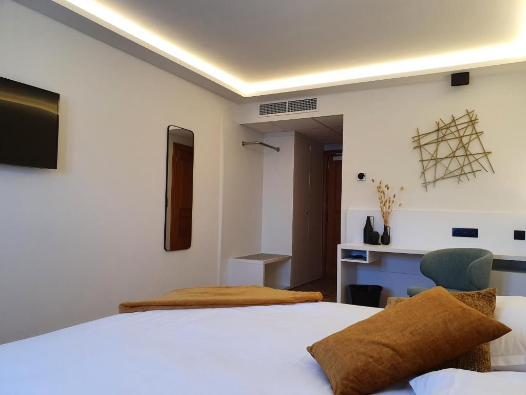 A hotel room with a bed, bedside table, mirror, and a wall-mounted air conditioning unit.