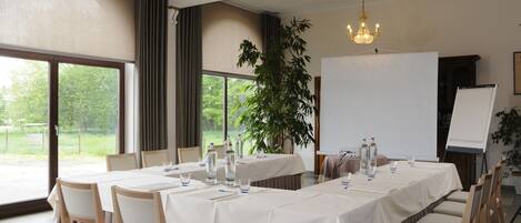 A conference room with a long table, chairs, a projector screen, and a large window with a view of greenery.