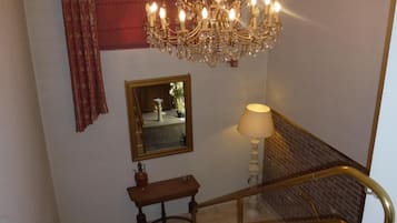 A staircase with marble steps, a brass handrail, a chandelier, a mirror, and a table with a lamp.