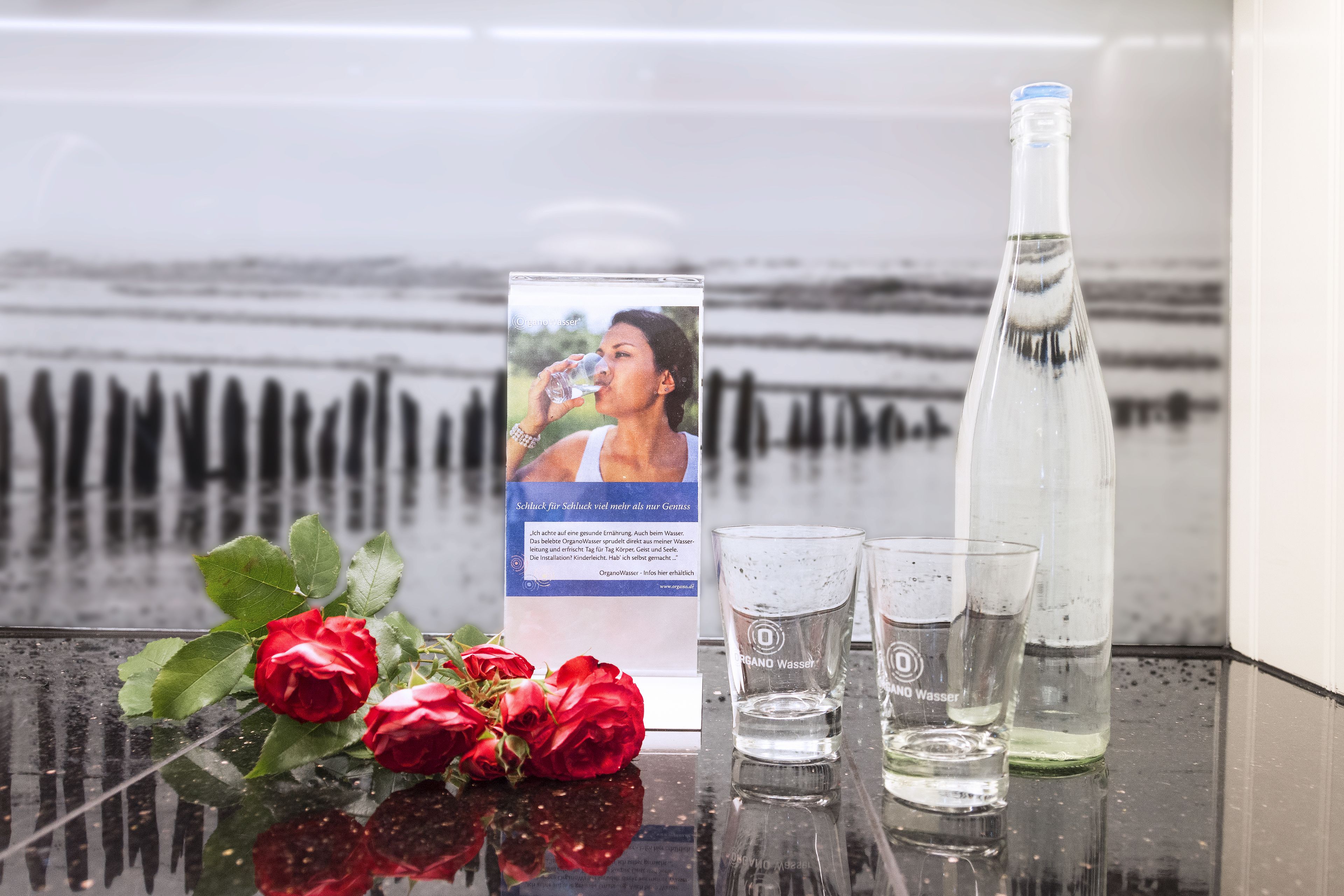 A table with a water bottle, two glasses, and a brochure with a woman drinking water.