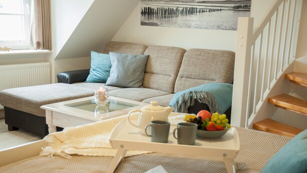 A cozy living room with a sofa, a coffee table with a tray, a book, and a bowl of fruit. - Freie Sicht Das Nordsee-Gesundheitshaus 1 (Dagebuell)
