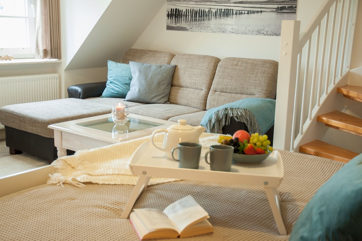 Un salon chaleureux avec un canapé, une table basse sur laquelle se trouve un plateau, un livre et un bol de fruits.