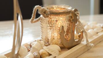 A decorative glass candle holder with a rope handle, surrounded by seashells on a wooden tray.