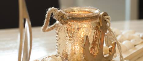 A decorative glass candle holder with a rope handle, surrounded by seashells on a wooden tray.