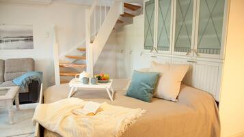 Ein Schlafzimmer mit einem Bett, einem Nachttisch mit Buch und Obstschale, einem Fenster mit Milchglas und einer Treppe.